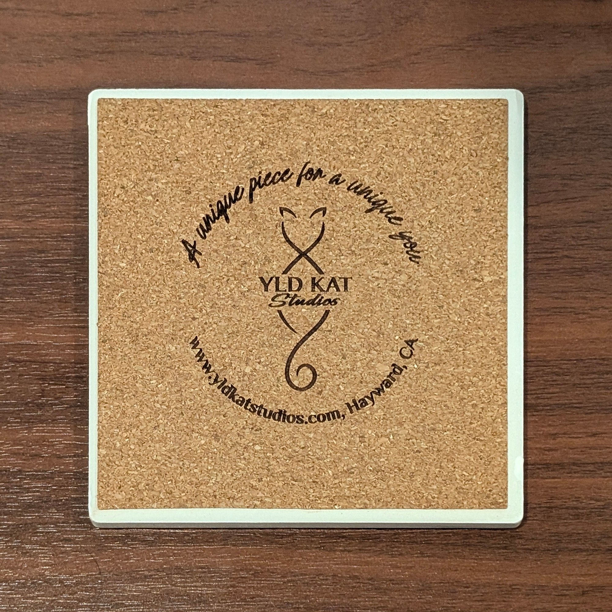 Cork back of a YldKat Studios square ceramic coaster, engraved with the YldKat logo, "A unique piece for a unique you" and yldkatstudios.com, Hayward, CA